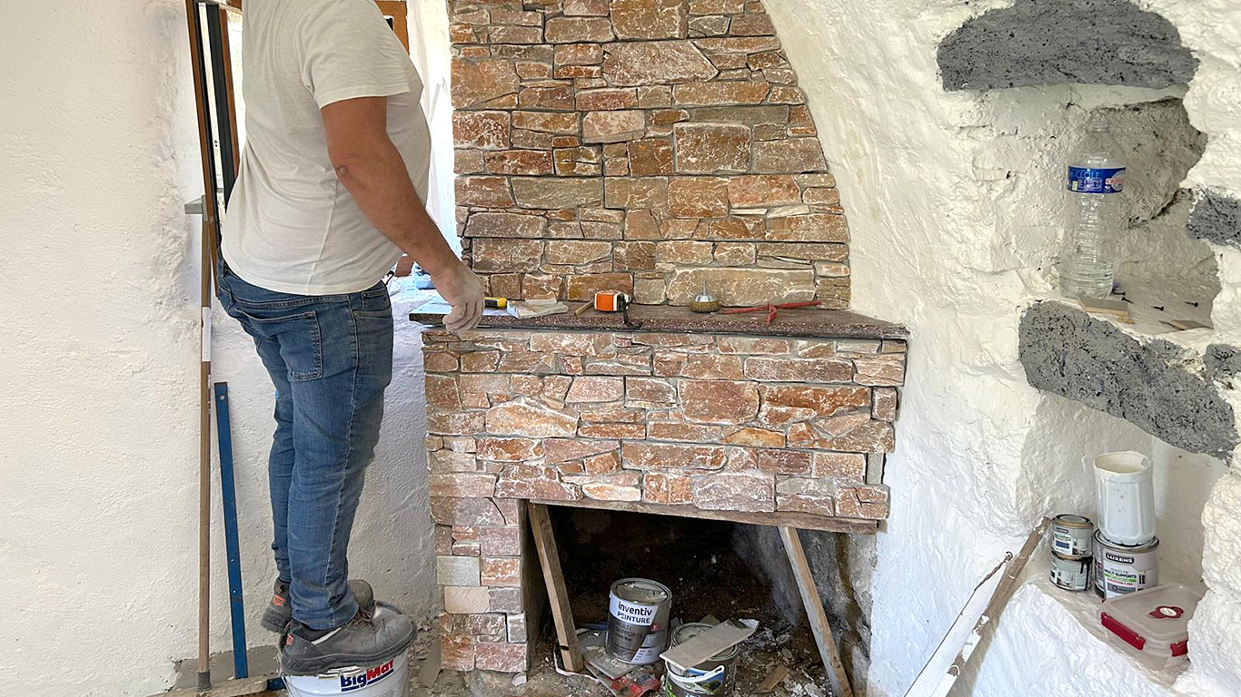 Pose d'un parement en pierres naturelles par un maçon pour la cheminée intérieure.